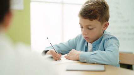 Sticker - Adorable caucasian boy student writing on notebook studying at classroom