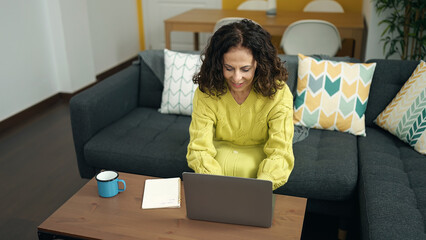 Canvas Print - Middle age hispanic woman using laptop sitting on sofa at home