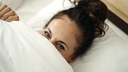 Canvas Print - Middle age hispanic woman lying on bed covering face with bedsheet at bedroom