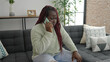 © Krakenimages.com - African woman with braided hair talking on the phone with worried expression at home