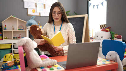 Sticker - Young beautiful hispanic woman preschool teacher having online lesson reading story book at kindergarten