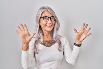 Canvas Print - Middle age woman with grey hair standing over white background showing and pointing up with fingers number ten while smiling confident and happy.