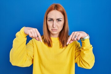 Sticker - Young woman standing over blue background pointing down looking sad and upset, indicating direction with fingers, unhappy and depressed.