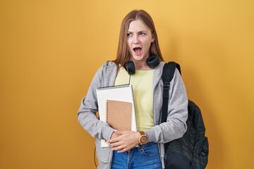 Canvas Print - Young caucasian woman wearing student backpack and holding books angry and mad screaming frustrated and furious, shouting with anger. rage and aggressive concept.