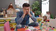 © Krakenimages.com - Young hispanic man preschool teacher stressed sitting on table at kindergarten