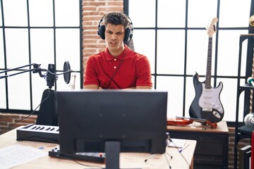 Sticker - Young hispanic man playing piano keyboard at music studio skeptic and nervous, disapproving expression on face with crossed arms. negative person.