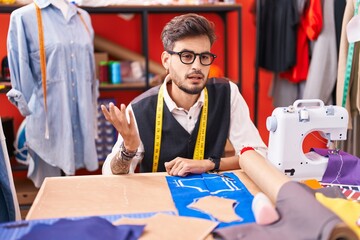 Poster - Young hispanic man tailor sitting on table speaking at atelier