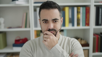 Sticker - Young hispanic man student sitting on table with doubt expression at library university