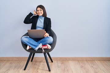 Sticker - Young hispanic woman sitting on chair using computer laptop smiling doing phone gesture with hand and fingers like talking on the telephone. communicating concepts.