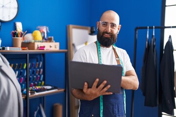 Poster - Young bald man tailor smiling confident using laptop at clothing factory