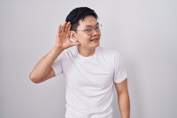 Sticker - Young asian man standing over white background smiling with hand over ear listening an hearing to rumor or gossip. deafness concept.