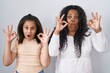 © Krakenimages.com - Mother and young daughter standing over white background looking surprised and shocked doing ok approval symbol with fingers. crazy expression