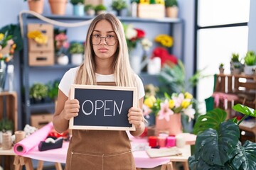 Poster - Young blonde woman working at florist holding open sign relaxed with serious expression on face. simple and natural looking at the camera.