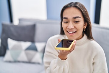 Poster - Young hispanic woman talking on the smartphone sitting on sofa at home