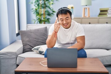 Sticker - Young chinese man using laptop at home smiling with an idea or question pointing finger with happy face, number one