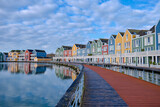 Fototapeta Tulipany - Houten, The Netherlands - April 25 2023. Wooden bridge alongside colourful wooden lakeside houses. Reflected in the water of lake De Rietplas. Diminishing perspective.