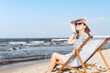 © rogerphoto - Happy brunette woman wearing sunglasses and hat relaxing on a wooden deck chair at the ocean beach