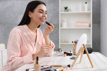 Poster - Beautiful young woman applying lipstick at dressing table indoors