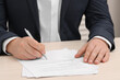 © New Africa - Man signing document at wooden table, closeup
