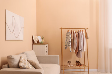 Poster - stylish living room interior with comfortable sofa and clothing rack