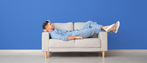 Wall Mural - Young man relaxing on sofa near blue wall