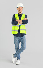 Wall Mural - Male worker in vest and hardhat on grey background