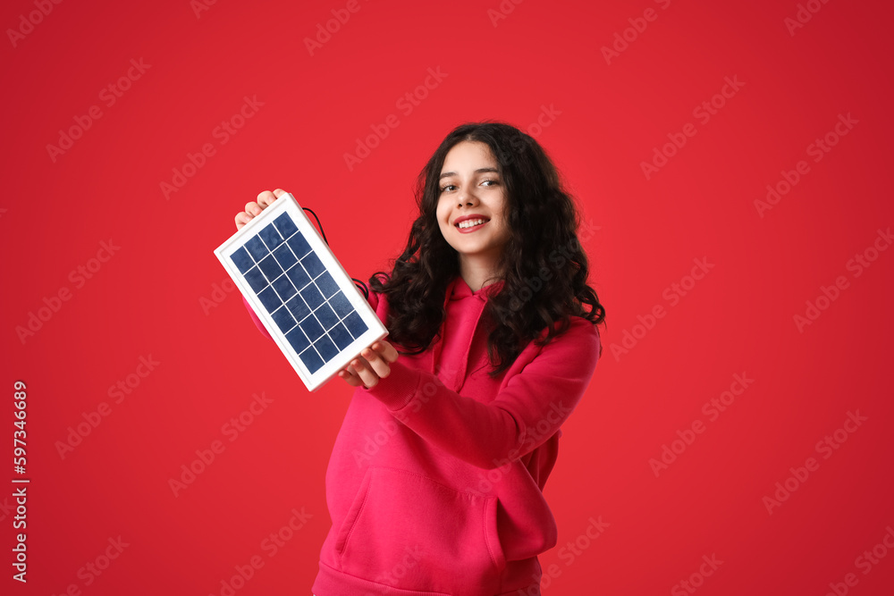 Teenage girl with portable solar panel on red background