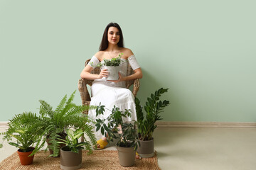 Canvas Print - Young woman with houseplants sitting in armchair near green wall