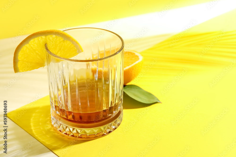 Glass of rum with orange slice on yellow background