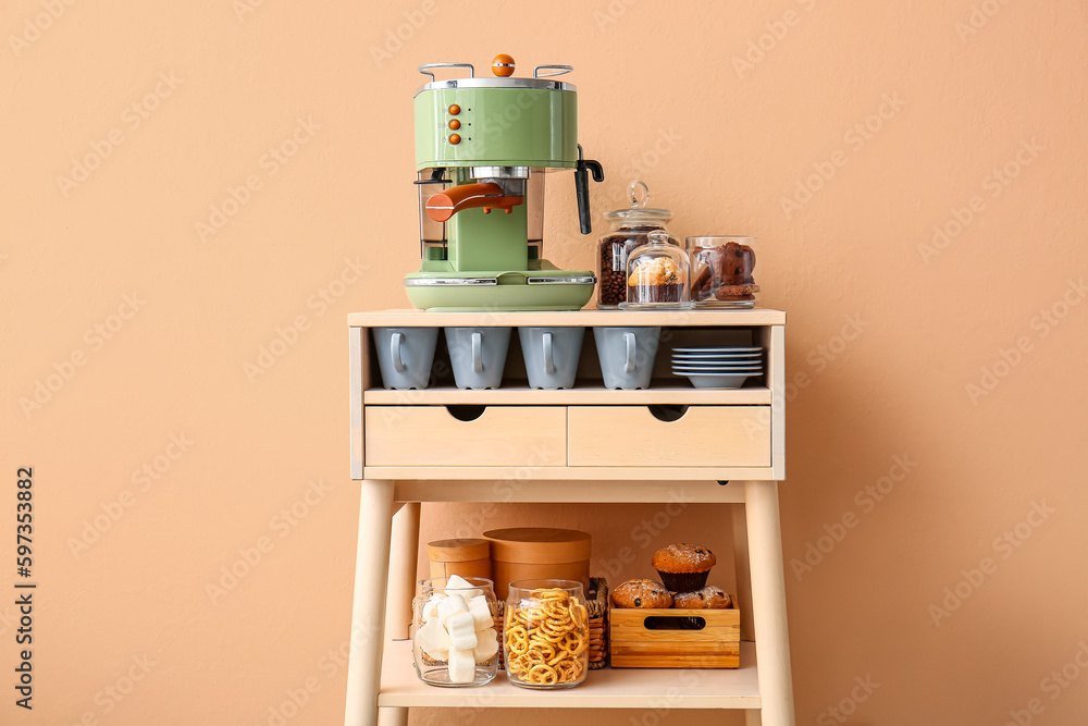 Table with coffee machine, snacks and cups near beige wall