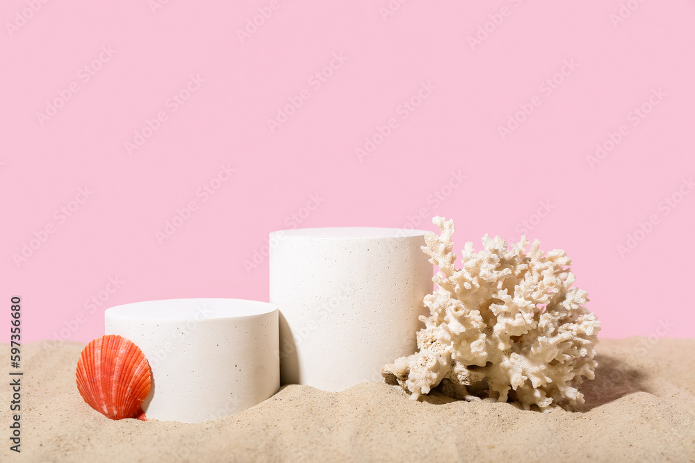 Decorative plaster podiums, seashell and coral in sand on pink background