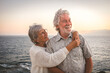 Cheerful romantic senior couple embraced at the sea at sunset light - old people outdoors enjoying vacations or retirement together