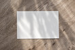 © Viktoriia - Blank paper card on neutral beige wooden desk background with floral sun light shadows, postcard template, mockup with copy space