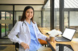 © Prathankarnpap - Confident asian female doctor in white coat and stethoscope using laptop in modern hospital canteen