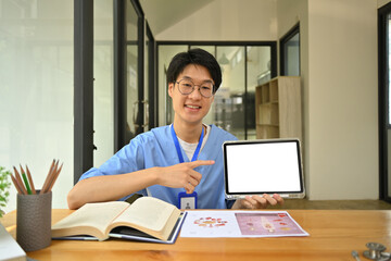 Young Asian male medical students wearing blue scrubs showing digital tablet and pointing at blank screen