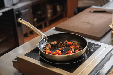 Wall Mural - Tomatoes and mushrooms is cooking in frying pan in restaurant kitchen