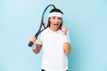 Wall Mural - Young tennis player woman isolated on blue background celebrating a victory in winner position