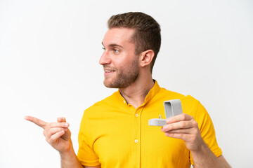 Wall Mural - Young man holding a engagement ring isolated on white background pointing to the side to present a product