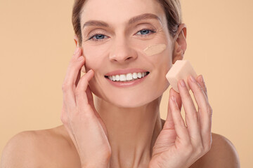 Wall Mural - Woman blending foundation on face with makeup sponge against beige background