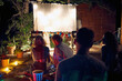 © luckybusiness - .Friends enjoying together outdoor at night and watching movie