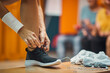 © luckybusiness - Young woman tying her shoe in gym locker room, with earphones and towel on bench, getting ready for workout.