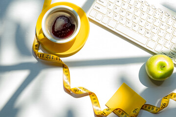 Wall Mural - Healthy snack with working in the office.  Fresh fruit apple and cup black coffee, tape measure for diet Health care with keyboard on white wood background.  Healthy Lifestyle Concept, top view.