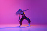 One young, attractive girl with dreadlocks dancing in street style over gradient purple neon background. Contemporary dance in motion