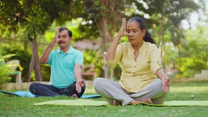 Wall Mural - Indian senior couple doing pranayama or nostril breathing yoga during morning at park - concept of mindfulness, relationship and healthy retirement lifestyle