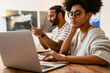 © Drobot Dean - African woman working on laptop while her husband using mobile phone sitting at table