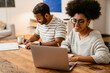 © Drobot Dean - Smiling african woman working on laptop while her husband writing down notes sitting at table