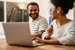 © Drobot Dean - Indian man smiling and looking at his wife while she working on laptop sitting at table