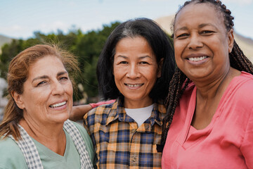 Wall Mural - Happy multiracial elderly friends smiling in front of camera - Portrait of senior women outdoor