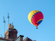 Hot air balloon rising above house roof tops clear sky