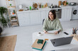 © LIGHTFIELD STUDIOS - Overjoyed freelancer holding notebook near gadgets and coffee at home.